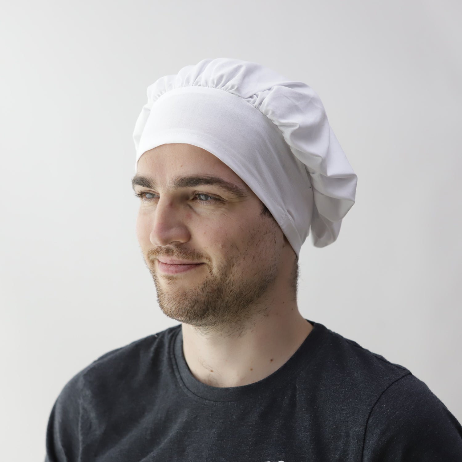 Person wearing a white chefs hat and a black T-shirt, facing slightly to the left, against a plain white background.