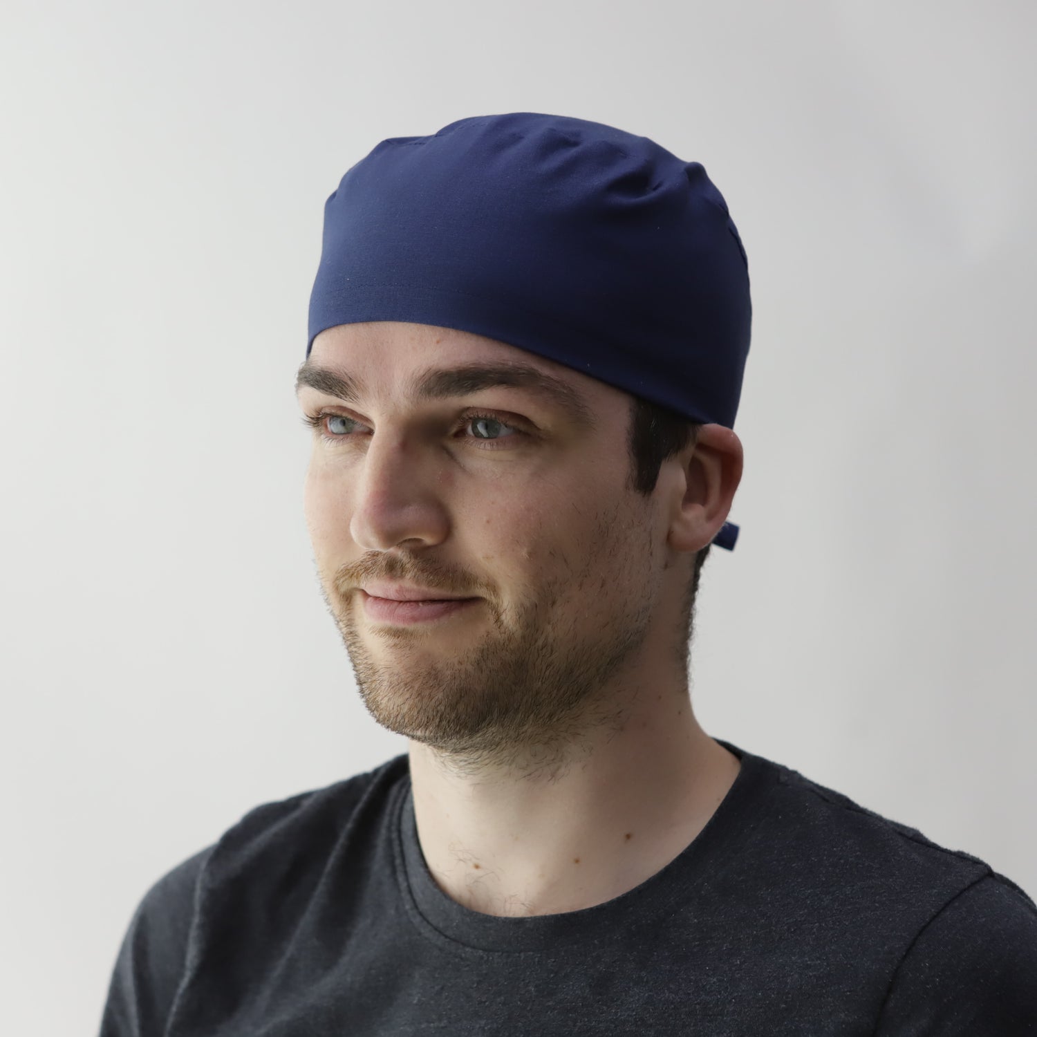 A person wearing a black shirt and navy blue headscarf looks to the side against a plain white background.