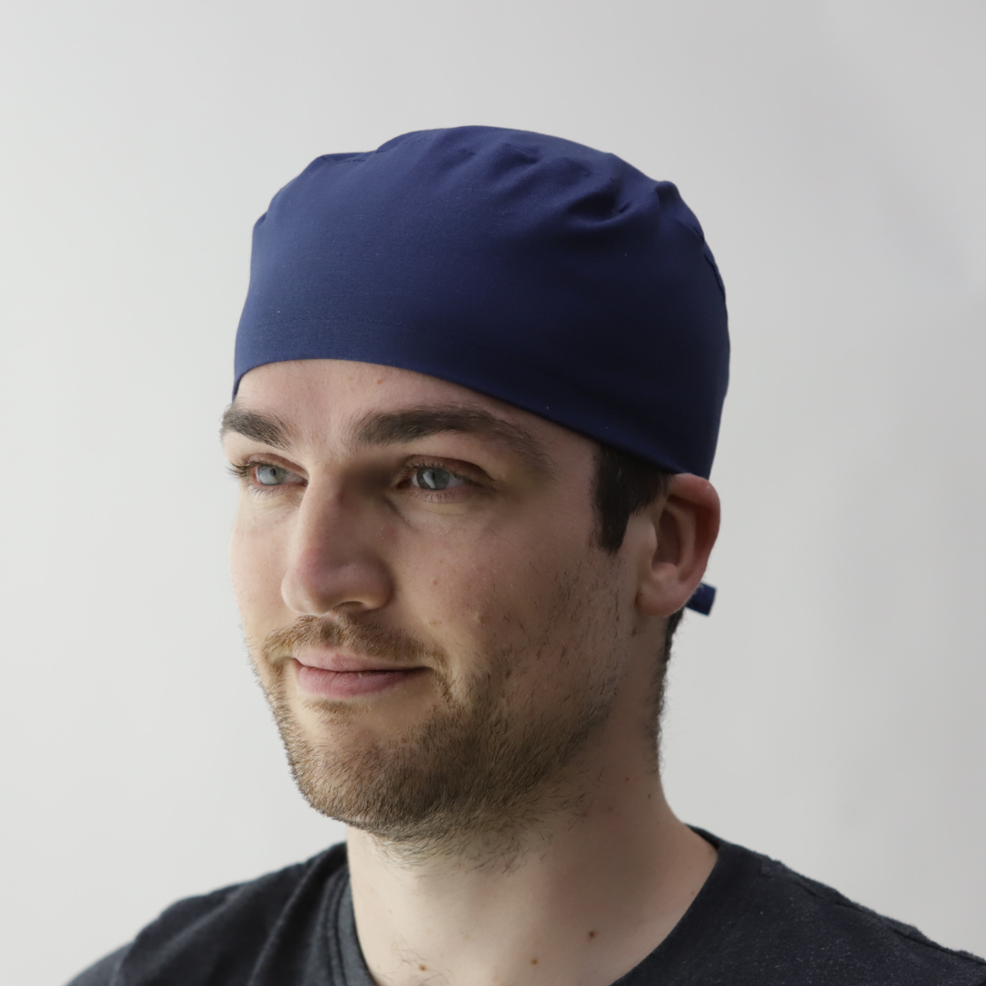 A man with a short beard wears a navy blue Medicus Captain Scrub Cap above the ears, paired with a dark shirt, against a white background.
