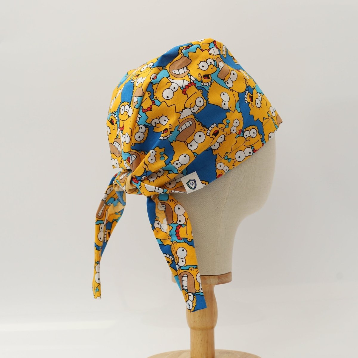 Back view of bright custom scrub cap featuring cartoon family characters with yellow faces on a blue background. Tie-back style scrub cap handmade by Medicus Caps for medical professionals seeking fun, colorful headwear.