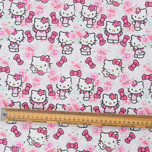 Close-up of Hello Kitty in pink rose garden print with bows and roses, fabric swatch with ruler for scale.