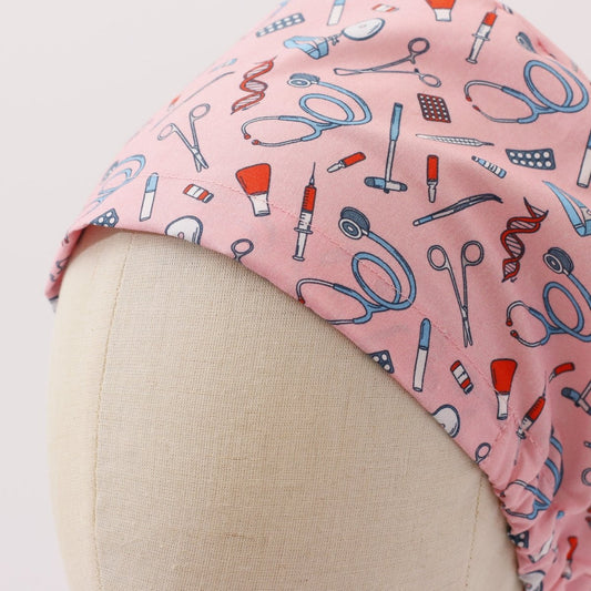 Custom pink scrub cap by Medicus Caps featuring illustrated medical tools like stethoscopes, syringes and scissors. Bouffant style surgical cap made to order.