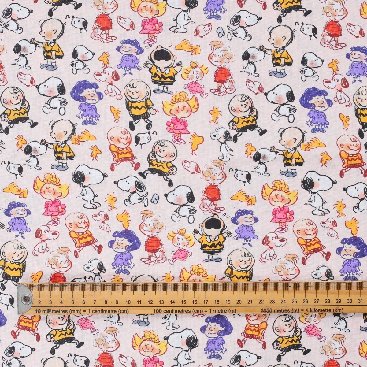 Close-up of fabric featuring Snoopy and Charlie Brown scribble-style cartoon characters with ruler for scale.