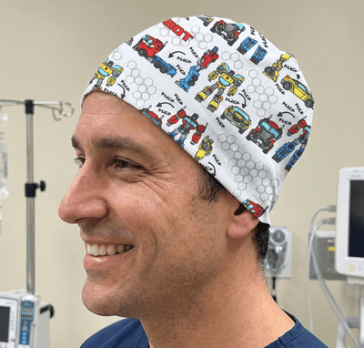 Colourful robot vehicles and machinery print scrub cap with white background worn by smiling healthcare professional