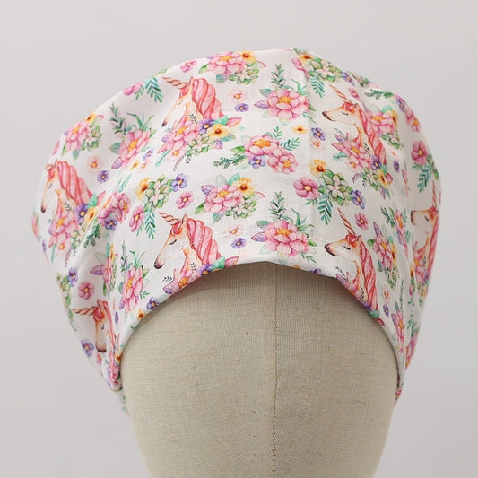 Bouffant style white custom scrub cap featuring pink unicorns and colorful floral patterns. Handmade unicorn floral scrub cap by Medicus Caps with roomy fit ideal for long hair or bouffant style.