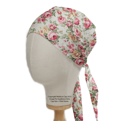 The Medicus Scrub Caps Floral Large Roses Vintage Ivory Scrub Cap, featuring a delightful pink and yellow floral pattern on white, is stylishly displayed on a mannequin. Tied back for adjustability, it offers an eco-friendly, sustainable choice for medical professionals.