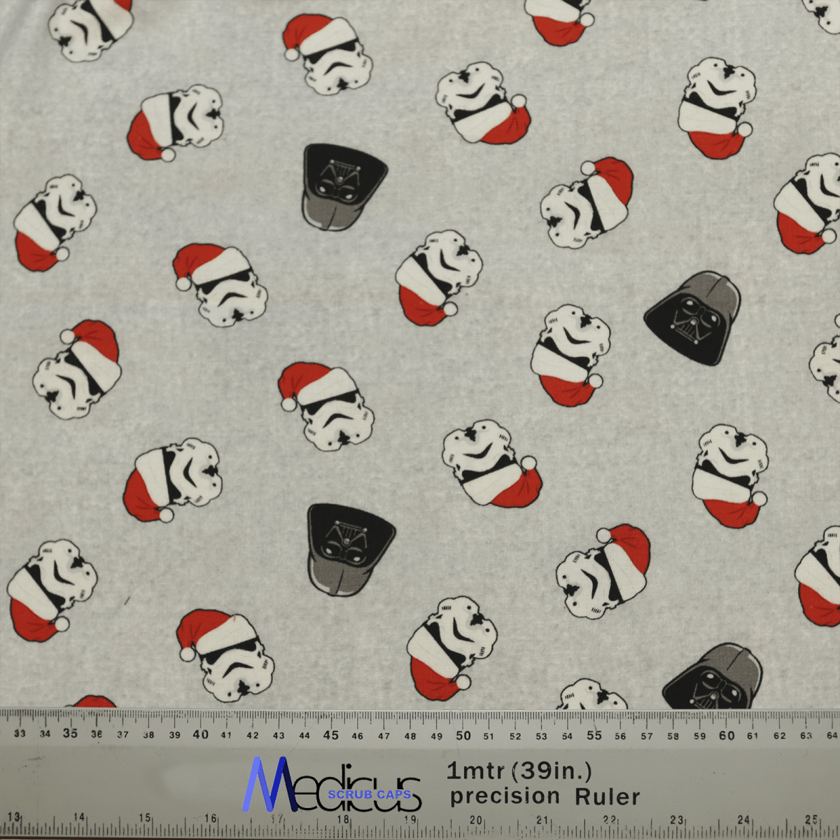 The Star Wars Christmas Darth Vader Scrub Cap by Medicus Scrub Caps features black helmets and stormtrooper helmets with Santa hats on a gray background. A ruler at the bottom shows inches and centimeters, ideal for measuring your creative festive projects.