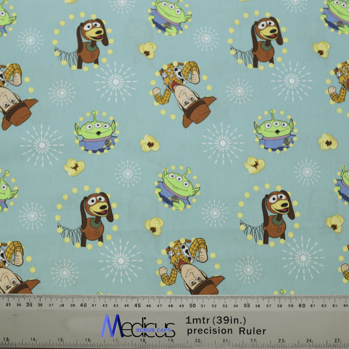The Toy Story Woody Slink Aliens Scrub Cap by Medicus Scrub Caps features a light blue fabric with playful cartoon characters, including a springy brown dog, cowboy, and green alien. Ideal for healthcare professionals, it includes whimsical starburst accents and a precision ruler for scale.