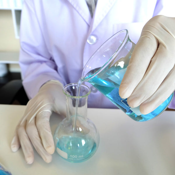 Laboratory technician in a white coat pouring blue liquid between glass flasks