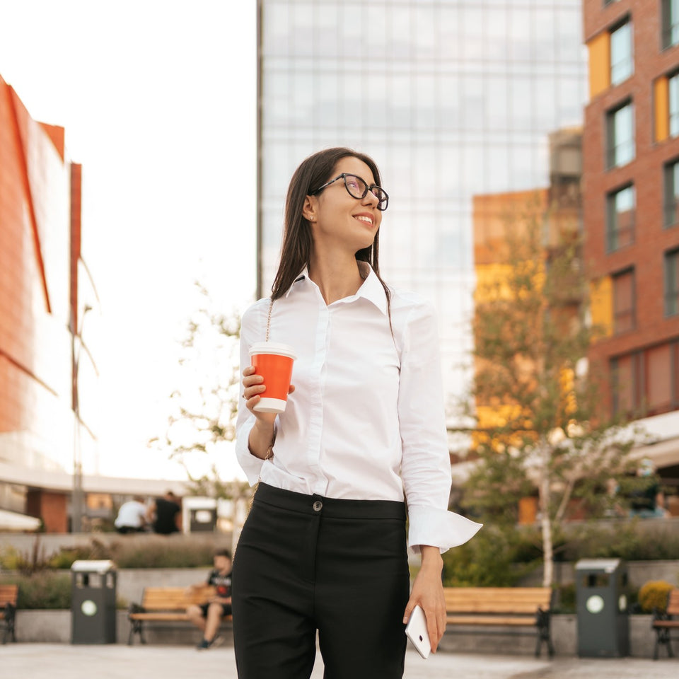 Professional woman in a white shirt walking to work with a coffee in the city