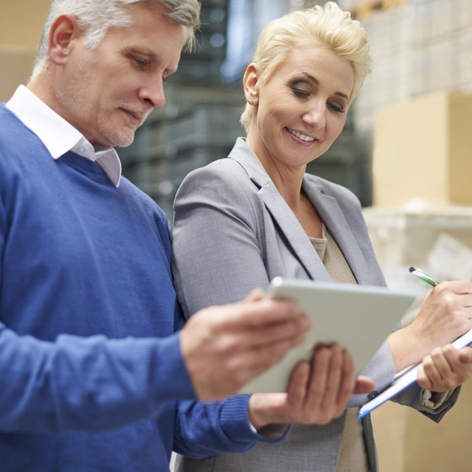 Two colleagues reviewing paperwork on a clipboard and tablet in a warehouse
