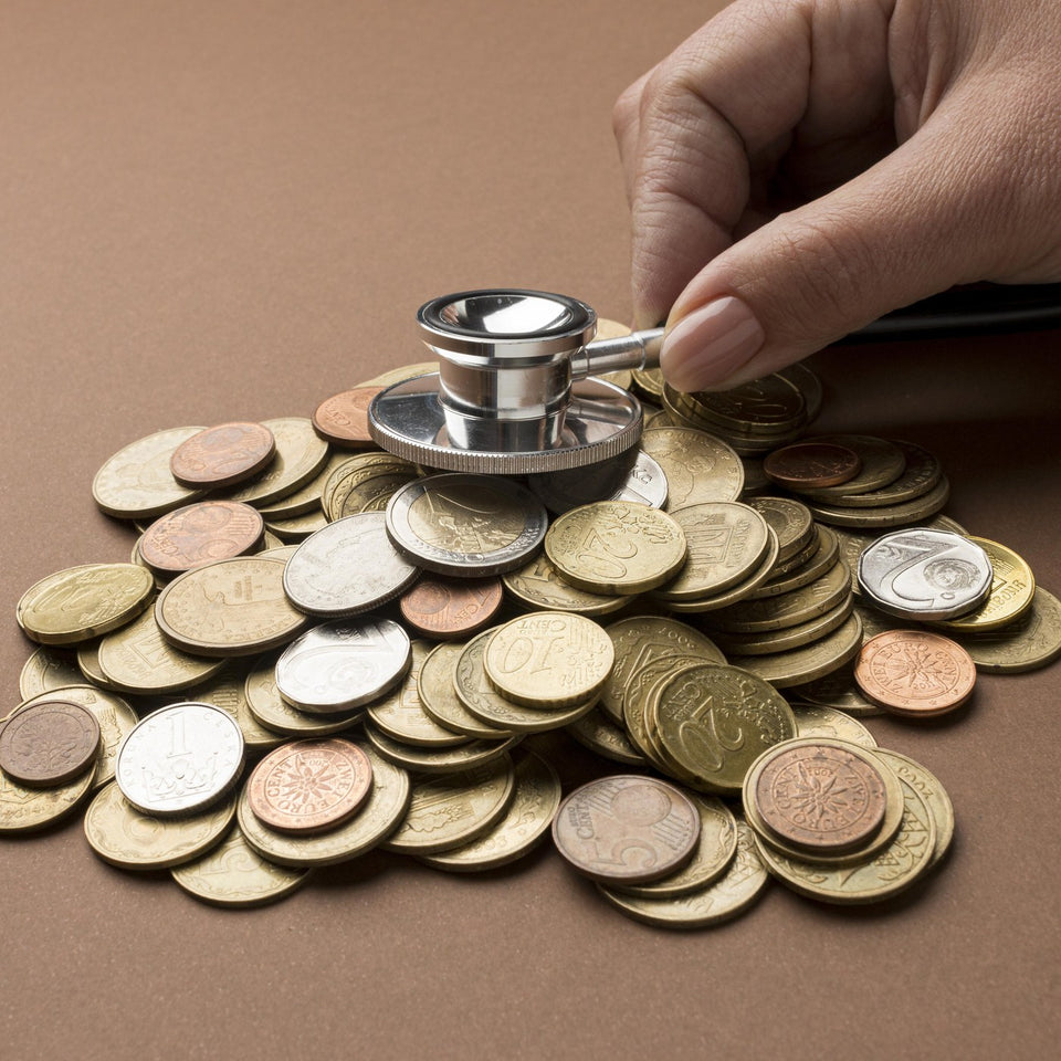 Hand placing a stethoscope on a pile of coins, representing healthcare costs