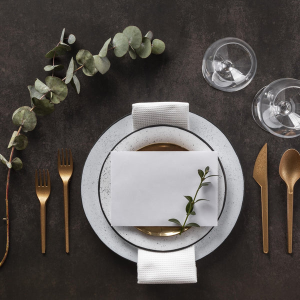 Elegant flat-lay dining table setting with plate, copper cutlery and glasses