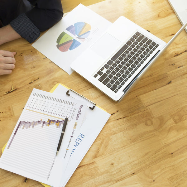 Laptop, charts and a report notebook on a wooden office desk