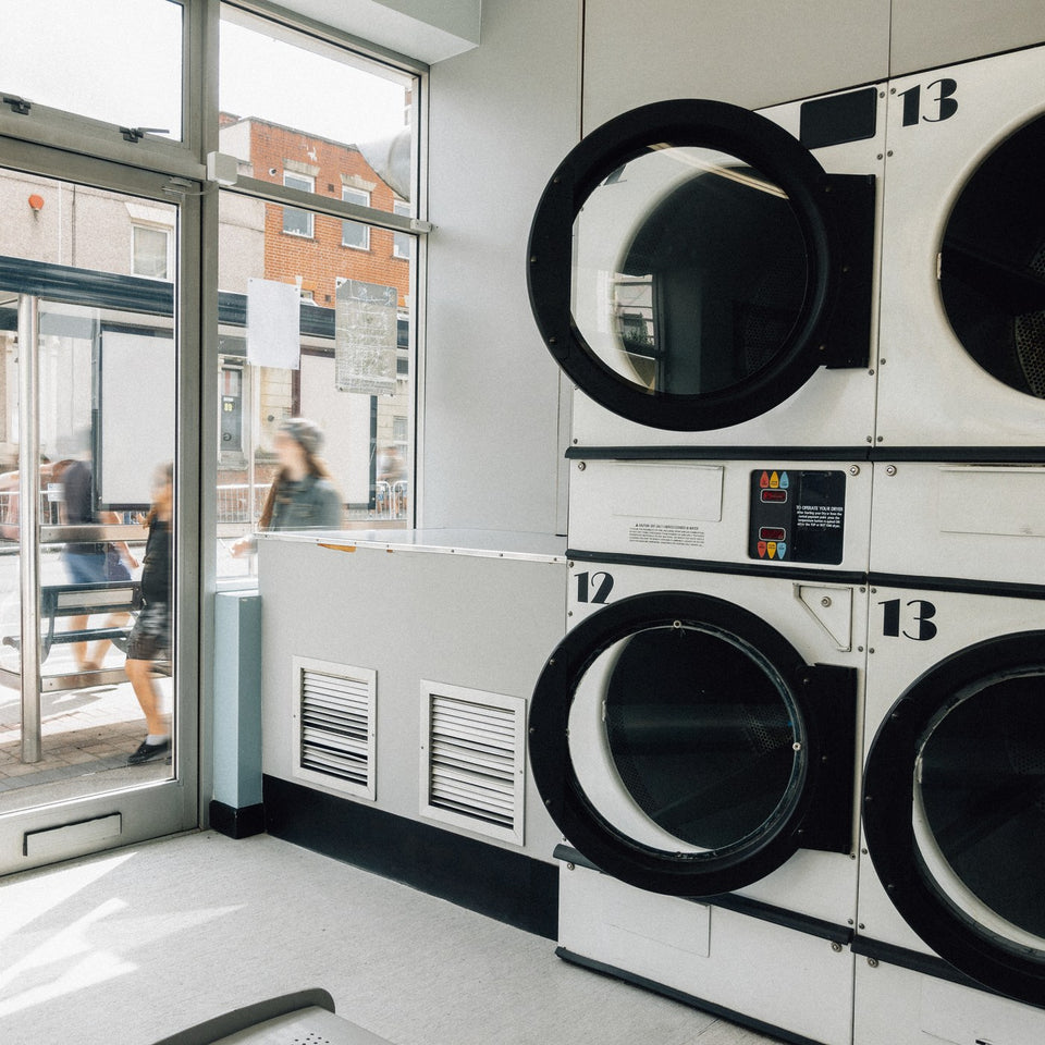 Row of front-loading washing machines in a laundromat by a window