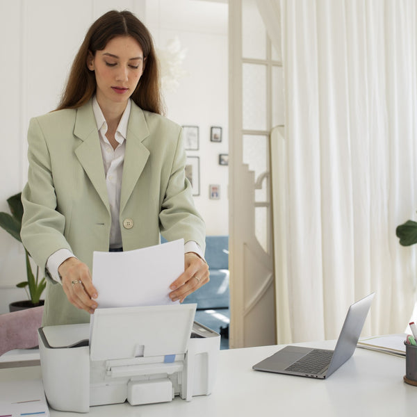 Woman using an office printer at a bright desk with a laptop