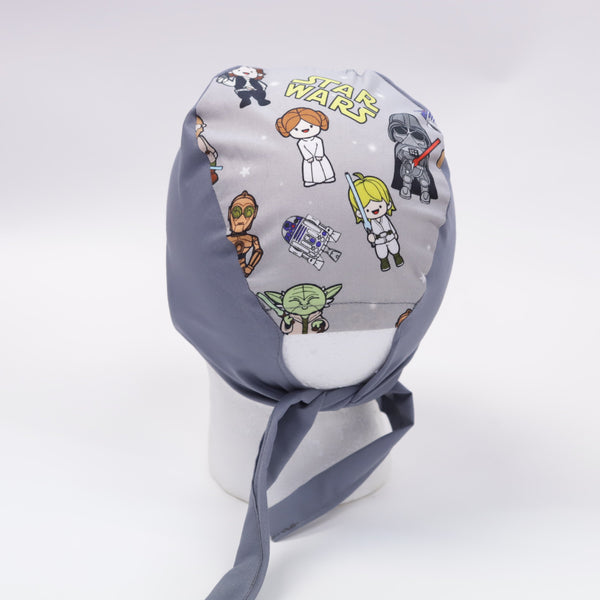 The Mullet scrub cap by Medicus Scrub Caps features Star Wars characters in a cartoon style with plain and patterned fabric. Ties at the back for comfort.