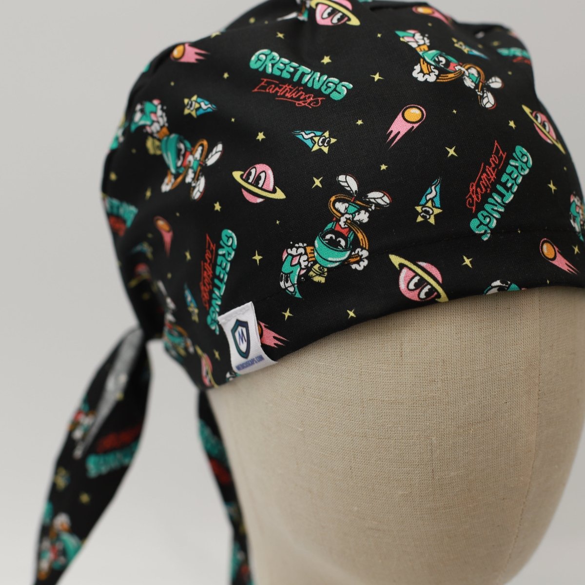 Custom black scrub cap by Medicus Caps featuring a space and alien theme with the words 'Greetings Earthlings' plus planets, rockets and aliens. Handmade surgical cap made to order.