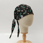 Side view of black custom scrub cap by Medicus Caps featuring a space and alien theme with 'Greetings Earthlings' text, planets, rockets and aliens. Long ties show back of cap; handmade surgical cap made to order.