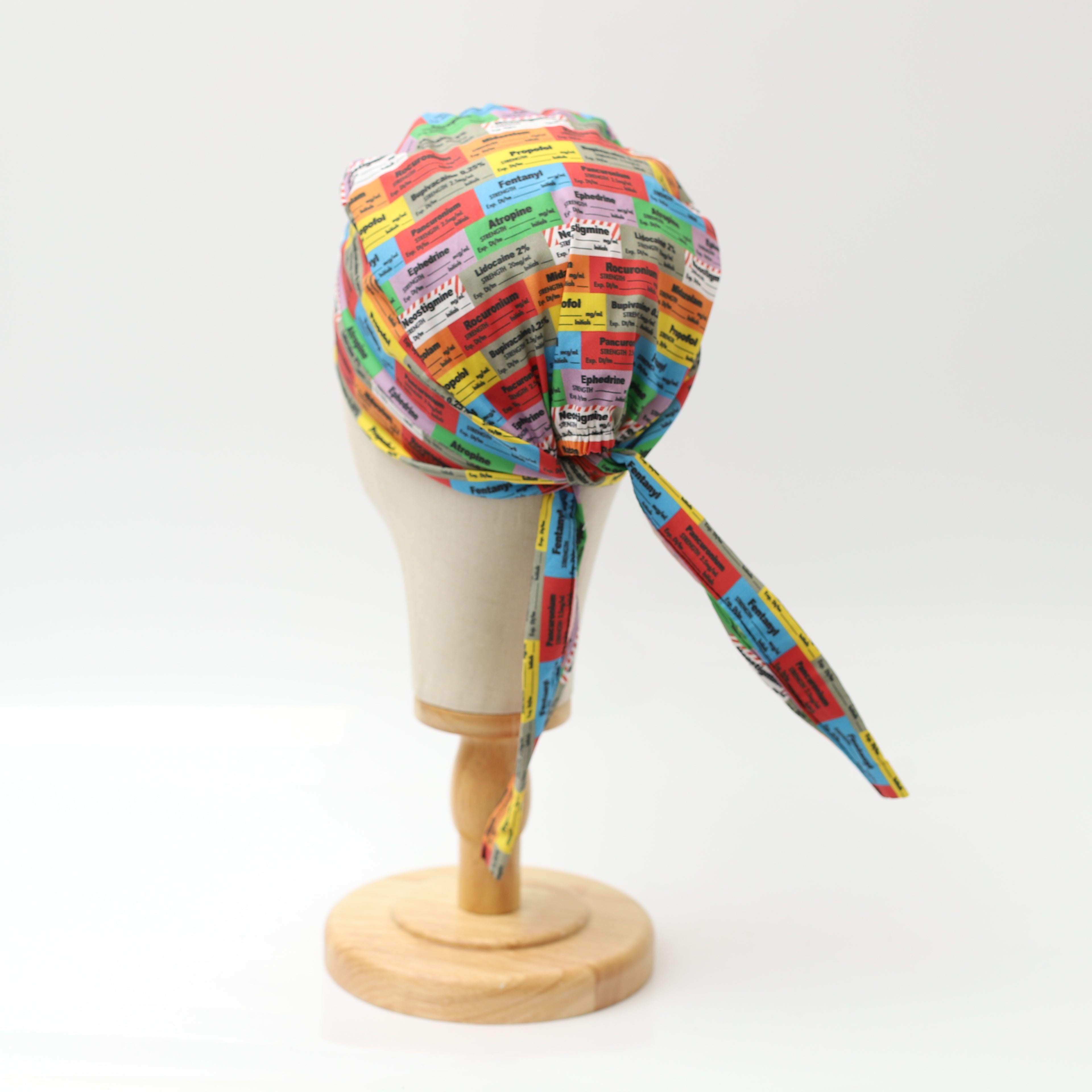 Medicus Scrub Cap featuring colorful anaesthetic drug labels, displayed on a mannequin head. Tied at the back for an adjustable fit.