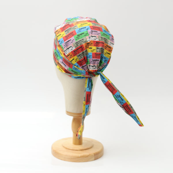 Medicus Scrub Cap featuring colorful anaesthetic drug labels, displayed on a mannequin head. Tied at the back for an adjustable fit.