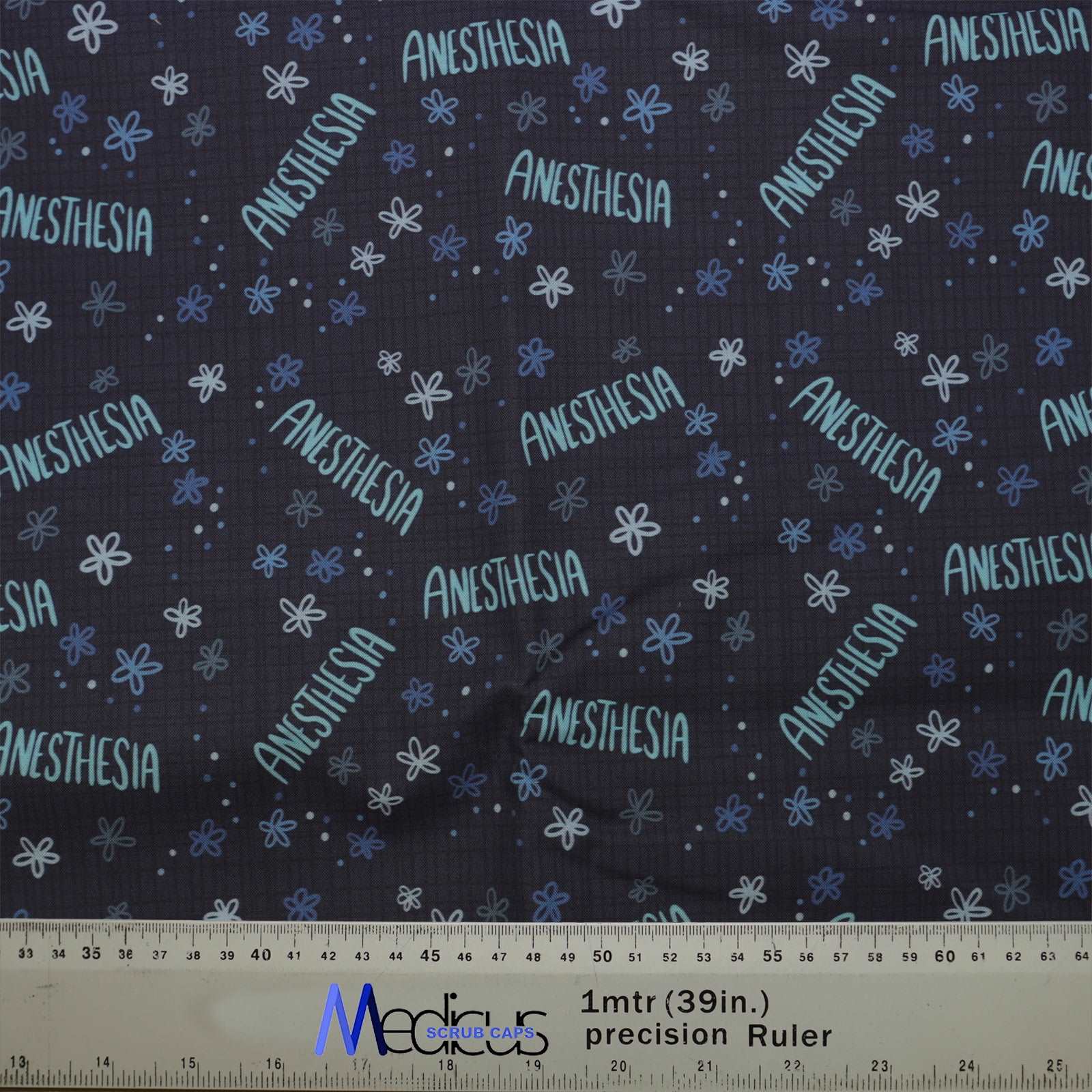 The Anaesthetist Anaesthesia Scrub Cap from Medicus Scrub Caps features "ANESTHESIA" in blue tones with small flowers, combining style and function. Ruler included for scale.