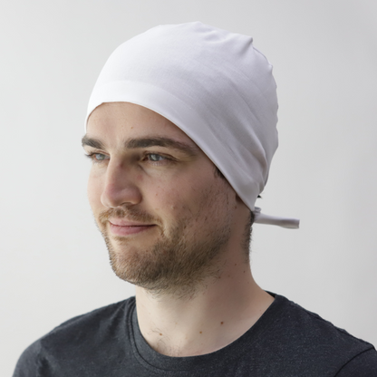 A person with a short beard wearing a white Medicus bandana scrub cap, tied at the back. They are dressed in a black t-shirt against a light gray background.