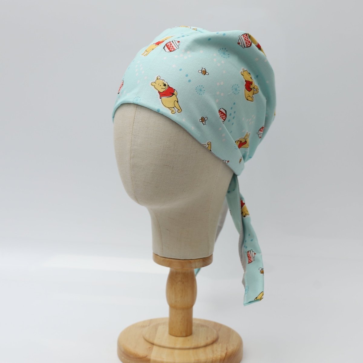 Custom blue scrub cap by Medicus Caps featuring cute bear and honey pot print. Side view shows long tie strap; handmade surgical cap made to order.