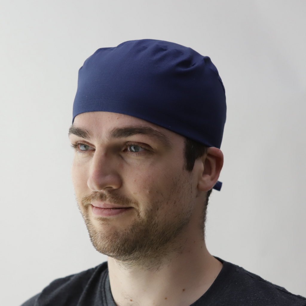 A man with a short beard wears a navy blue Medicus Captain Scrub Cap above the ears, paired with a dark shirt, against a white background.