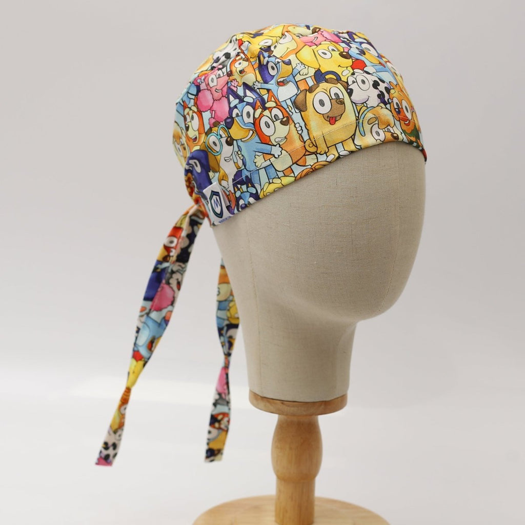 Custom scrub cap by Medicus Caps featuring colorful cartoon animals and characters on a white background; front view on mannequin with long tie straps.