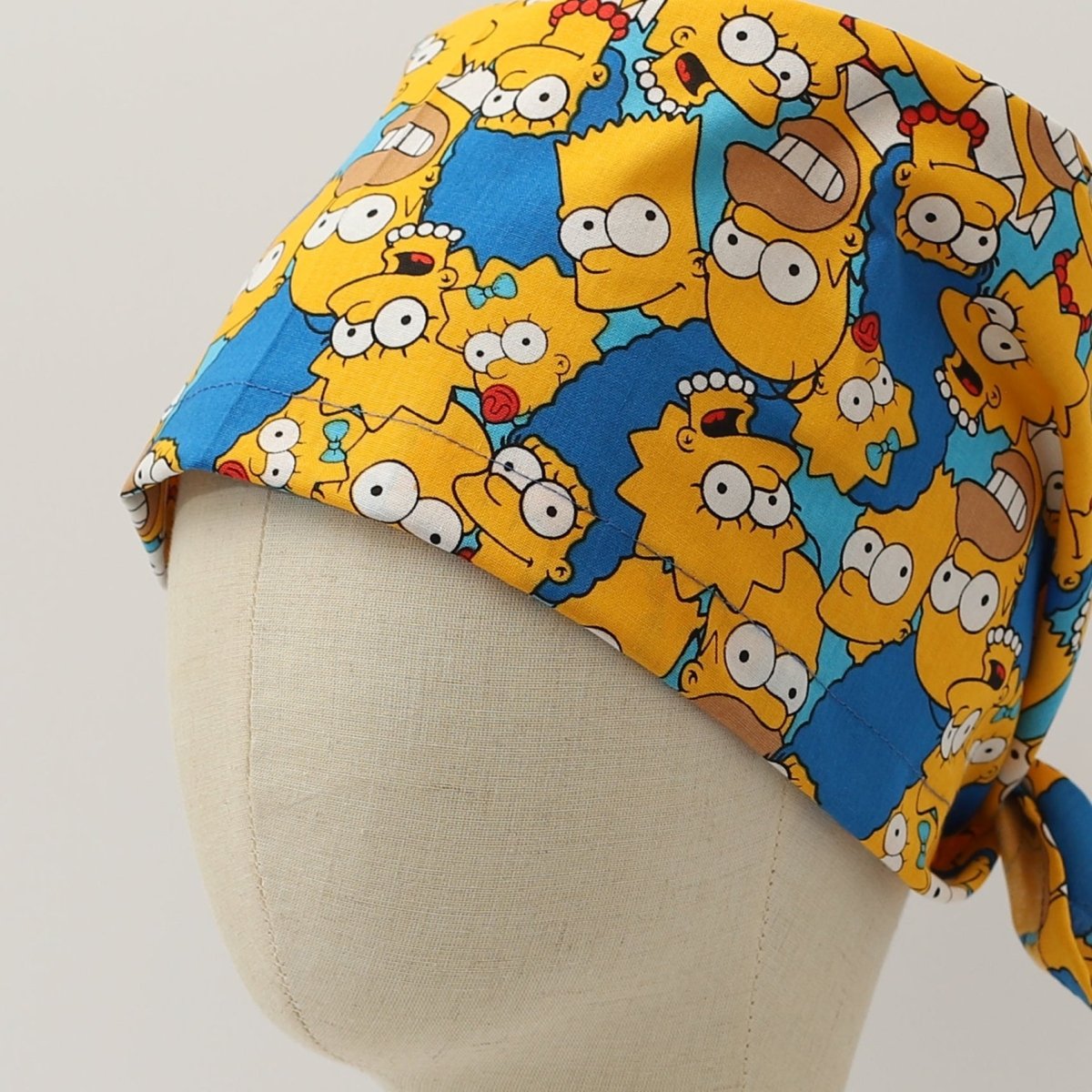 Bright custom scrub cap featuring cartoon family characters with yellow faces and blue background. Handmade by Medicus Caps with tie-back design for comfortable fit in medical settings.