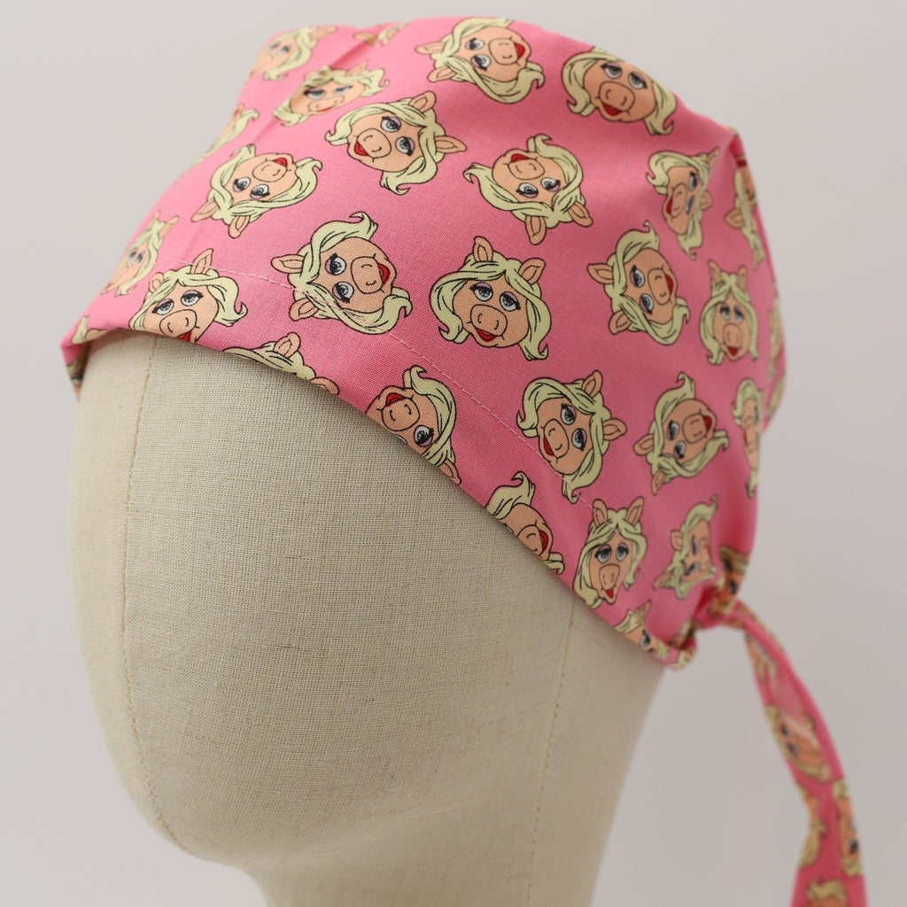 Custom pink scrub cap featuring cartoon pig faces pattern, handmade by Medicus Caps, tie-back style.