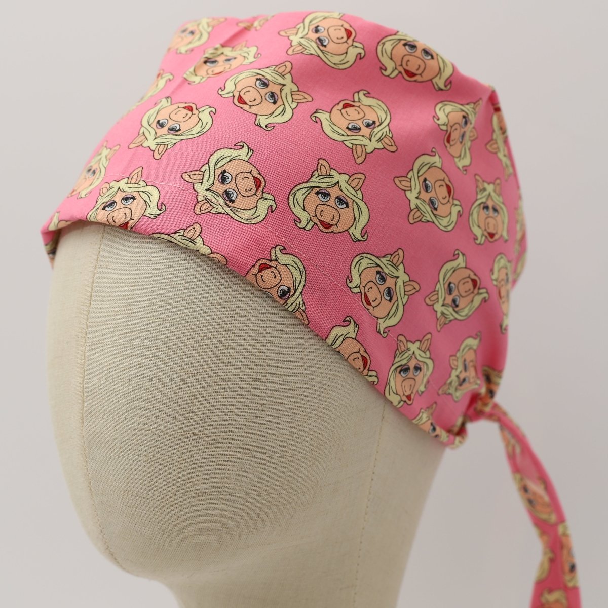 Custom pink scrub cap featuring cartoon pig faces pattern, handmade by Medicus Caps, tie-back style.