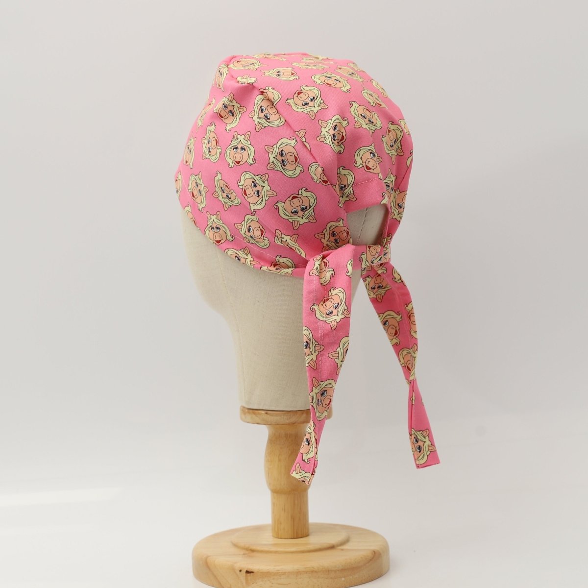 Back view of a custom pink scrub cap featuring cartoon pig faces pattern with long tie strap, handmade by Medicus Caps.