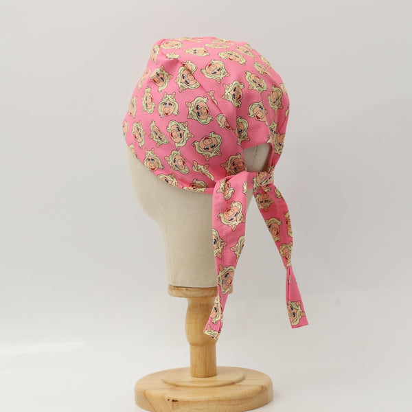 Back view of a custom pink scrub cap featuring cartoon pig faces pattern with long tie strap, handmade by Medicus Caps.