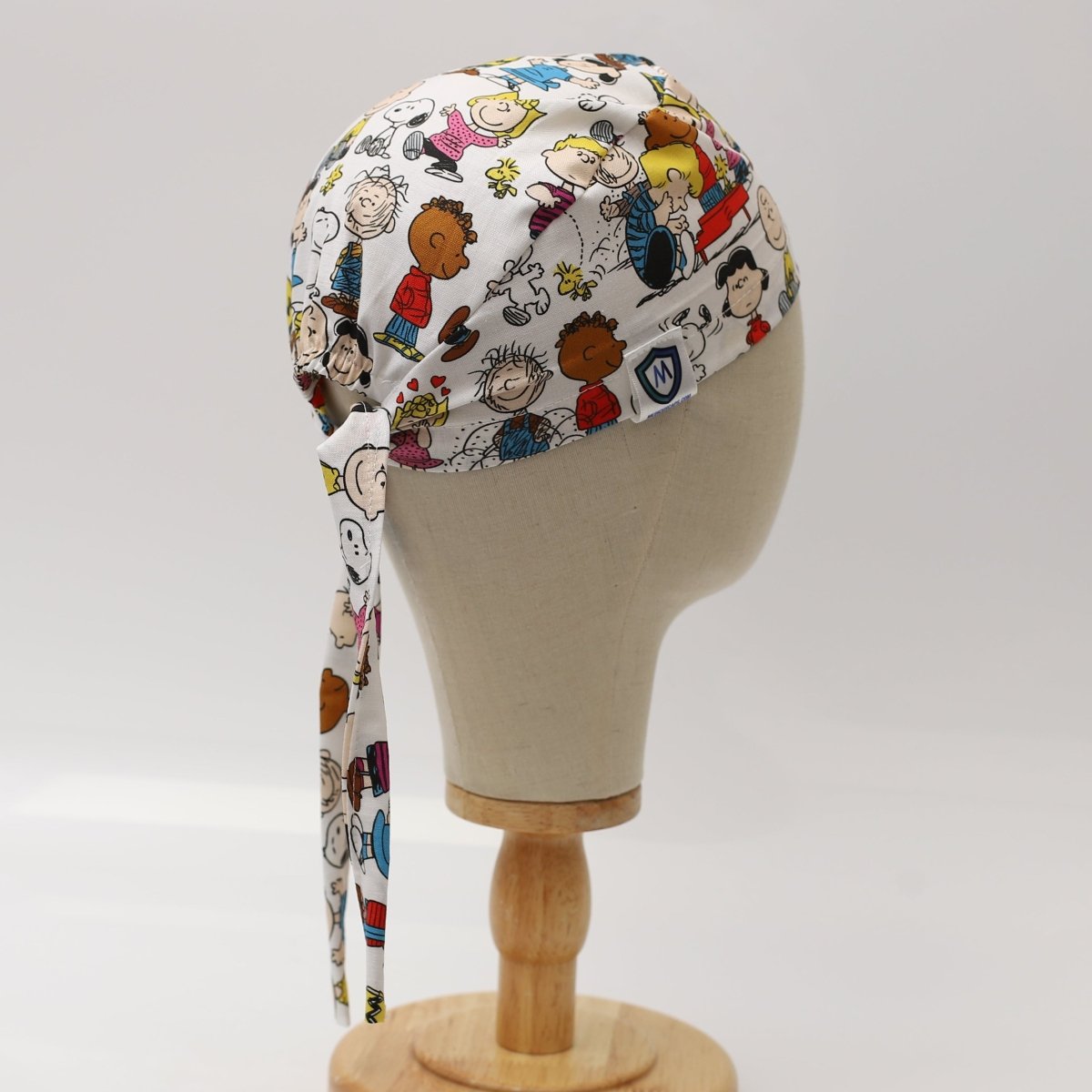Custom scrub cap by Medicus Caps featuring colourful cartoon character print on white fabric. Side view with long tie strap; handmade surgical cap made to order.