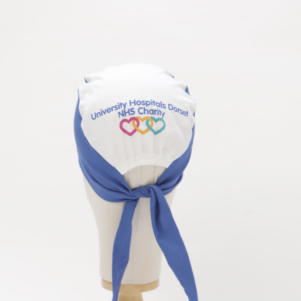 Mannequin head wearing a Medicus Scrub Cap with a white top, blue ties, and 'University Hospitals Dorset NHS Charity' text with heart logos.