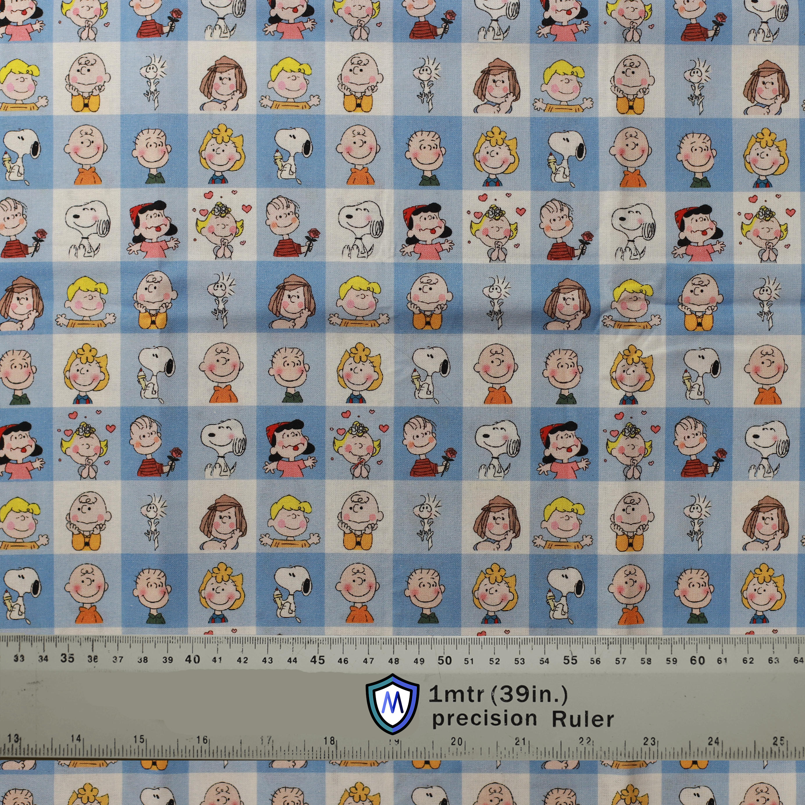 Fabric sample for Medicus Scrub Caps featuring Charlie Brown characters in a blue grid pattern. 1-meter ruler included for scale.