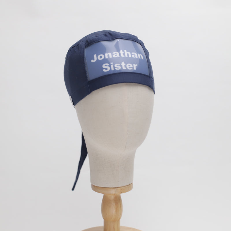 A mannequin head displaying a navy blue surgical cap with the text Jonathan Sister printed in white on the front. The cap has a tied back section and is placed on a wooden stand against a plain white background.