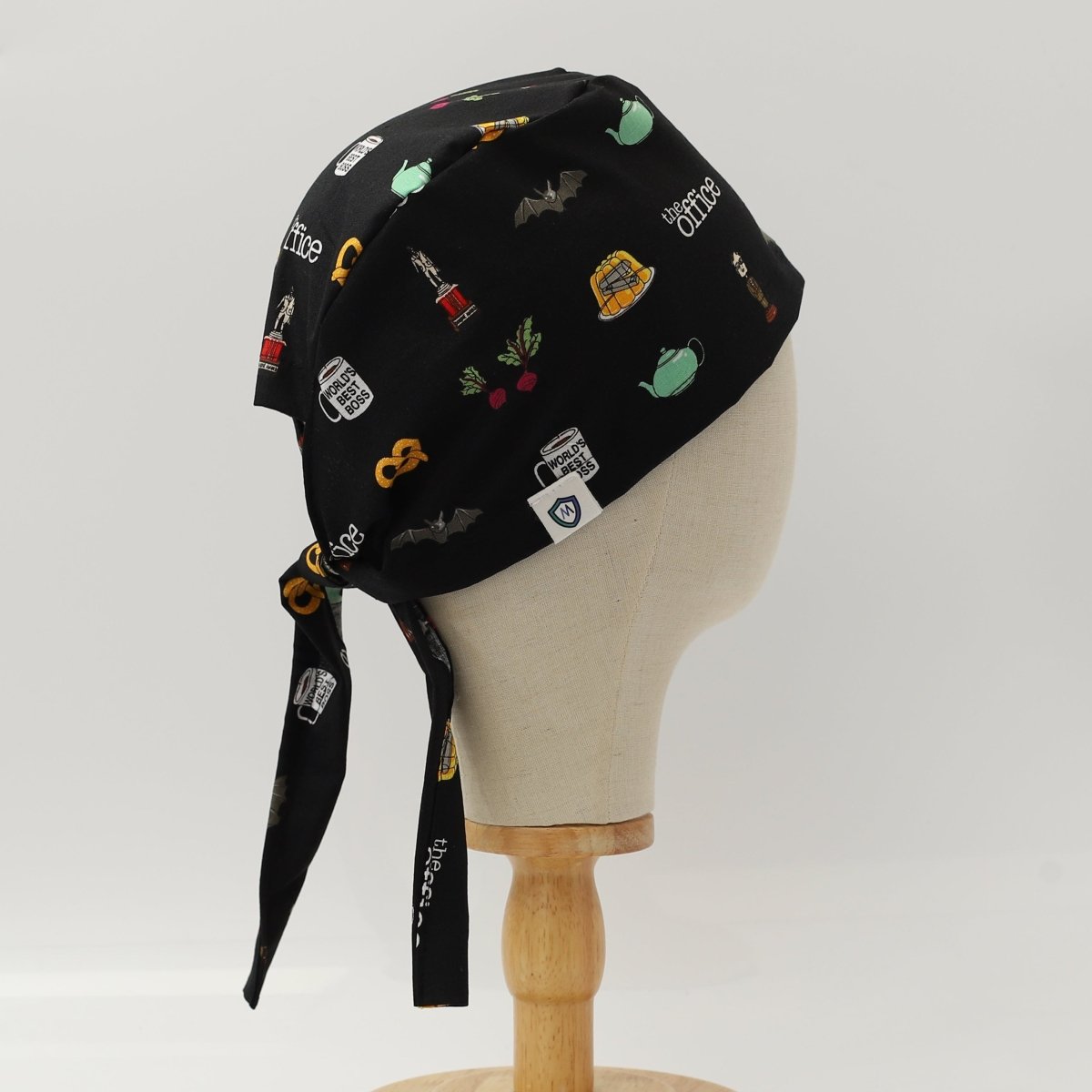 Side view of black custom scrub cap featuring coffee and tea-themed illustrations including French press, teapots, grinders and cups. Handmade coffee barista scrub cap by Medicus Caps with tie-back design ideal for medical professionals who love coffee.