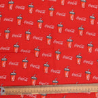 Coca-Cola fabric with red background and product pattern, ruler at the bottom.