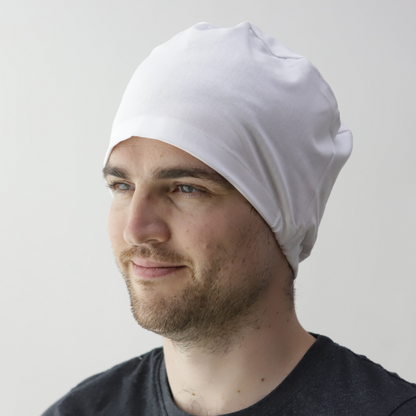 A person in a white Medicus Scrub Caps elastic-backed scrub cap, wearing a black shirt, gazes to the side with a slight smile against a plain background.