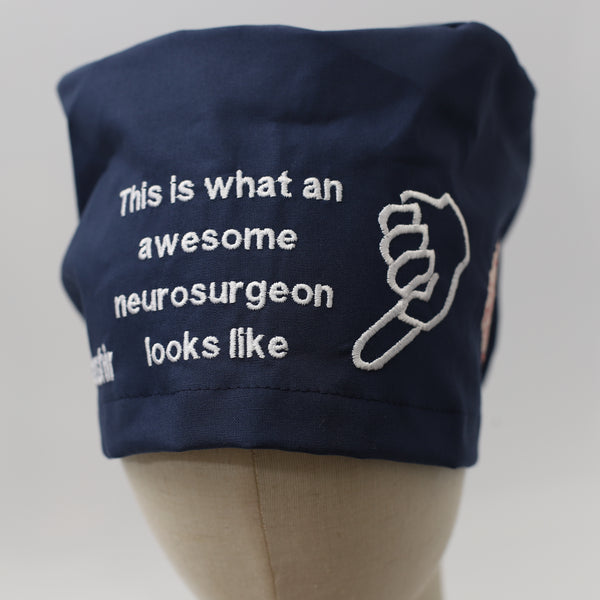Navy blue Medicus Scrub Cap with white embroidery reading "This is what an awesome neurosurgeon looks like" alongside a pointing hand design.
