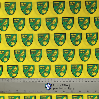Fabric sample for Medicus Scrub Caps featuring Norwich City FC crests in green and gold on a yellow background, with a 1-meter ruler for scale.
