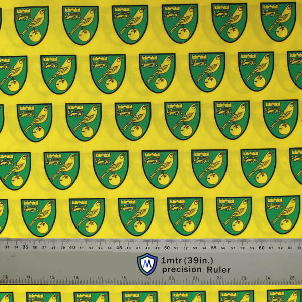 Fabric sample for Medicus Scrub Caps featuring Norwich City FC crests in green and gold on a yellow background, with a 1-meter ruler for scale.
