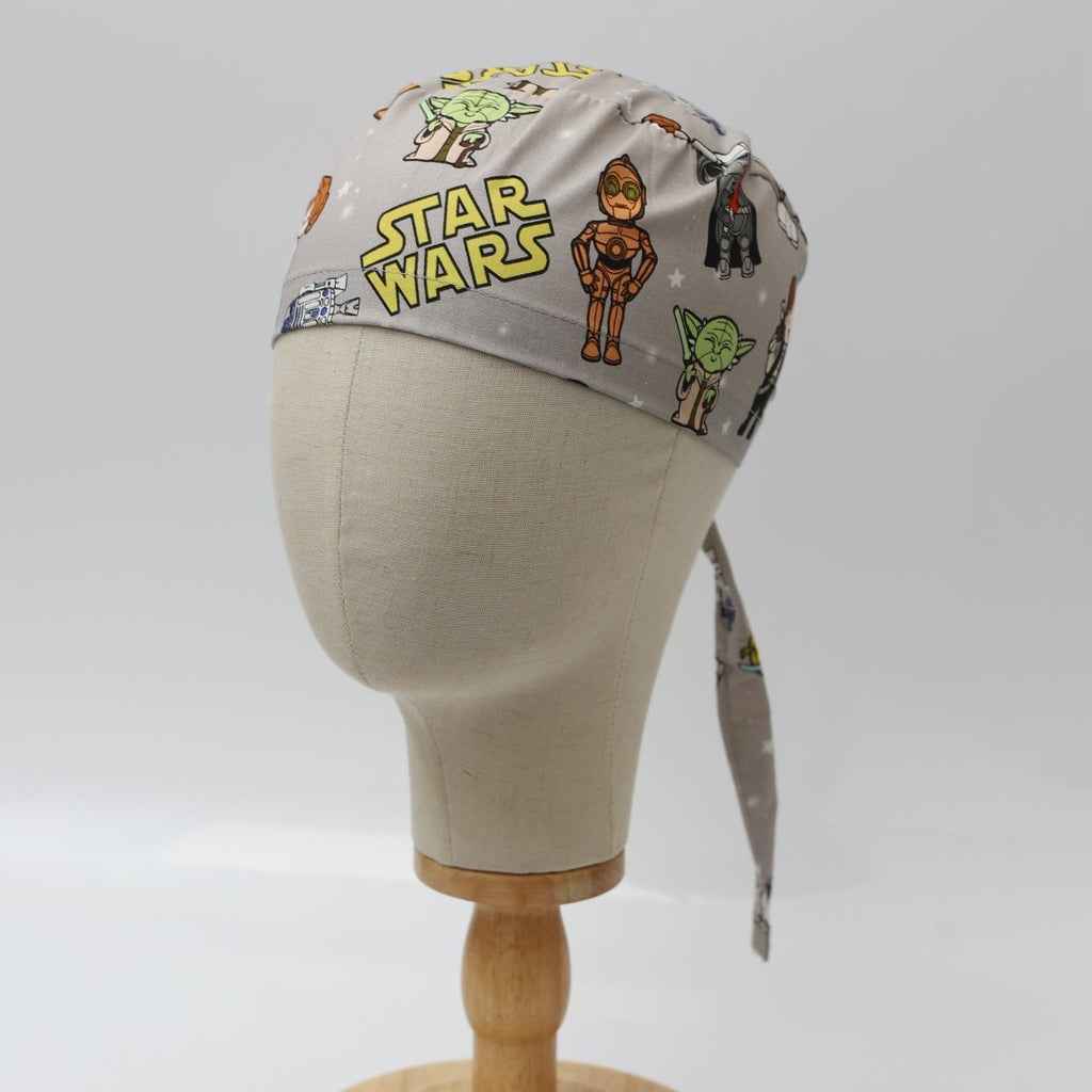 Custom grey scrub cap by Medicus Caps featuring cartoon galaxy heroes and robots print; side/front view on mannequin with ties.