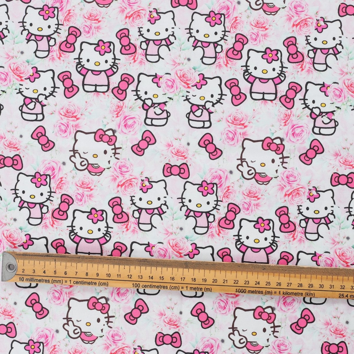 Close-up of Hello Kitty in pink rose garden print with bows and roses, fabric swatch with ruler for scale.