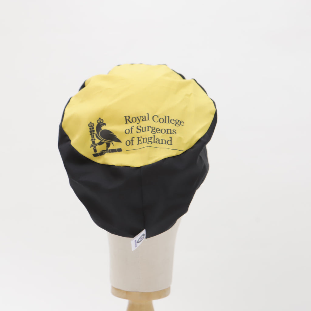 A Mullet Version scrub cap by Medicus Scrub Caps, custom printed in black and yellow with the Royal College of Surgeons of England logo, displayed on a mannequin.