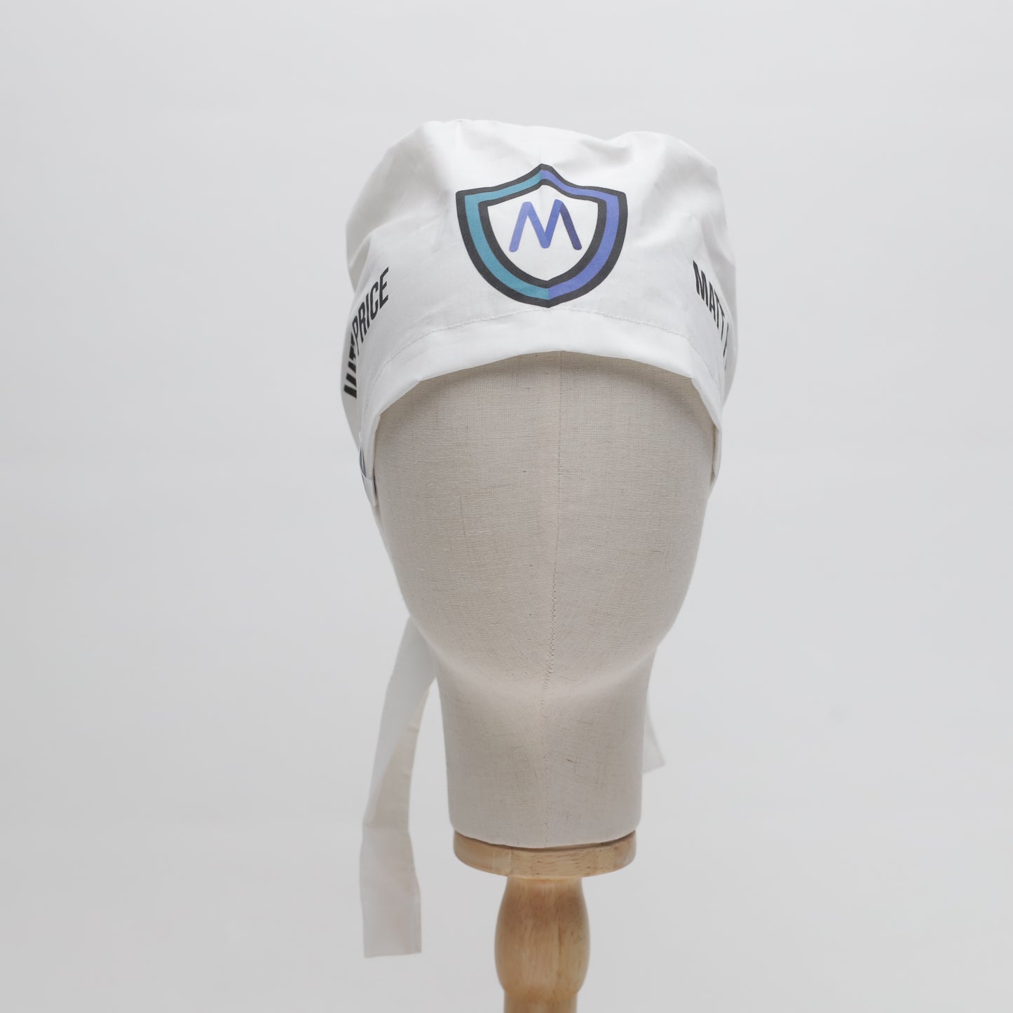 A mannequin head displays the Medicus Scrub Caps Specific Custom Printed Placement Scrub Cap, featuring a white design with an "M" logo and side text.