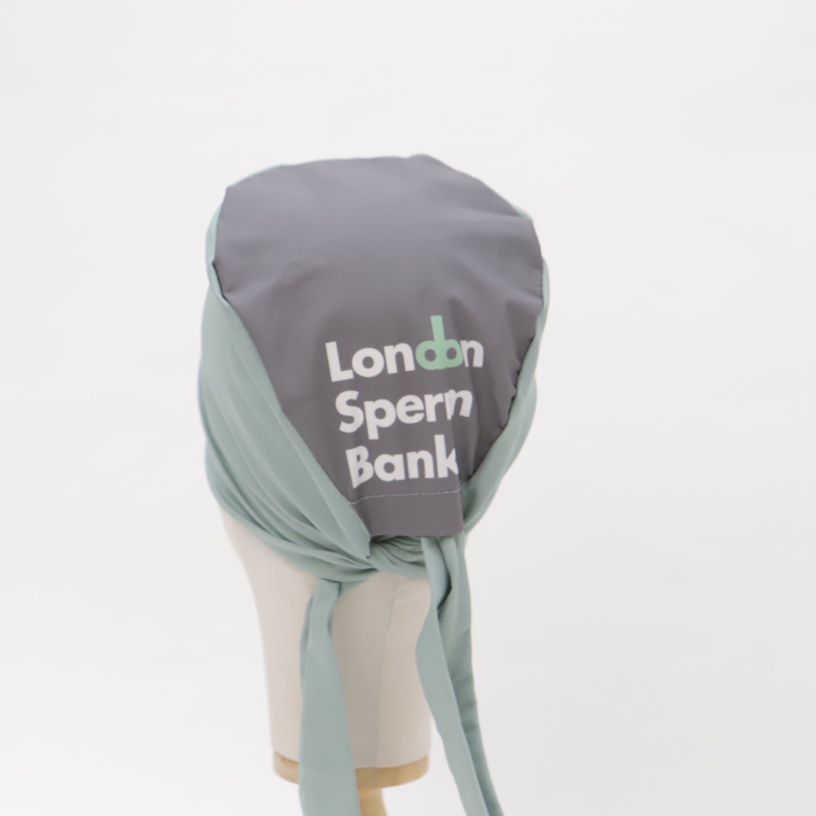 Grey and green Medicus Scrub Cap on a mannequin, featuring "London Sperm Bank" text. A custom-printed "make-your-own-custom-printed-mullet-scrub-cap" design.